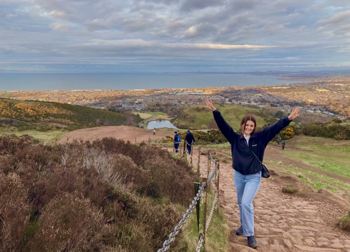 A student poses in Holyrood Park in Edinburgh, Scotland. A view of the city can be seen in the background.